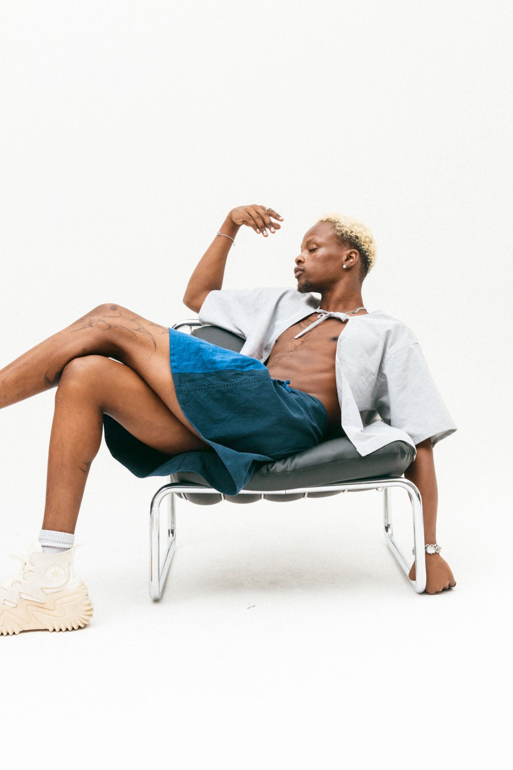Person sitting on a modern chair wearing the lani blue shirt and lani blue skirt against a white background